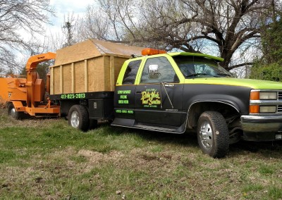 Green and black dump truck for Odd Jobs & Dirty Work Tree Service of the Missouri areas of Carthage, Joplin, Webb City and Oronogo on the job site cleaning up tree limbs and brush. The truck has the Company's phone number 417-825-2013, as well as some of the services that they offer; stump grinding, hauling, brish work. They are also licensed bonded and insured.